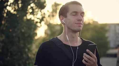 Young Man Enjoys Listening to Music on Headphones Using His Smartphone at Sunset in the City