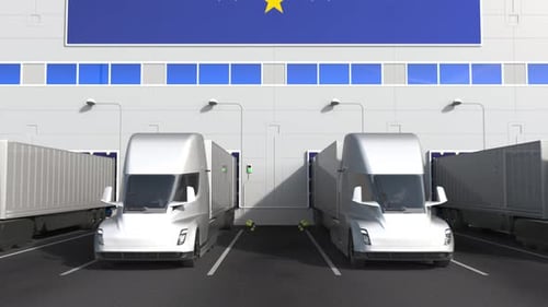 Camiones eléctricos en el muelle de carga del almacén con bandera de la UE