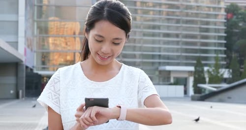 Woman Checks Smartwatch and Cellphone in City