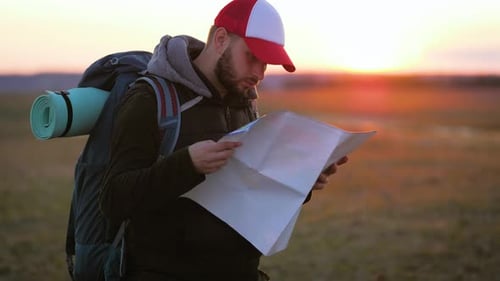 Hiker Looking at Map in Field at Sunrise