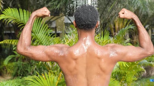 Shirtless Man Showers Outdoors in Tropical Setting