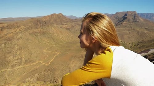 Blonde Schönheit lehnt sich über Geländer und genießt die Landschaft Gran Canarias