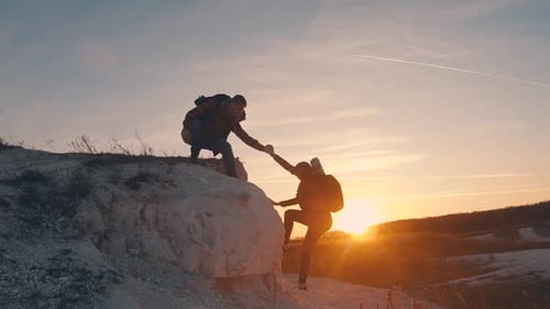 Man Helping Friend Climb Hill at Sunset
