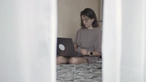 Frau sitzt auf dem Bett und arbeitet aus der Ferne