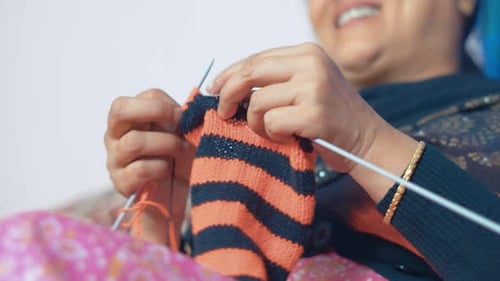 Happy woman knitting a red and black scarf with pleasure. Close up 4k of knit work tie-up hand work