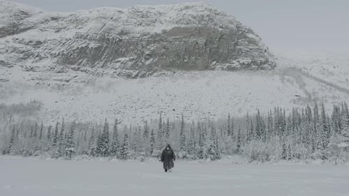 Ein Mann in einem schneebedeckten Mantel und einer Schutzmaske geht vor dem Hintergrund durch die Schneeverwehungen