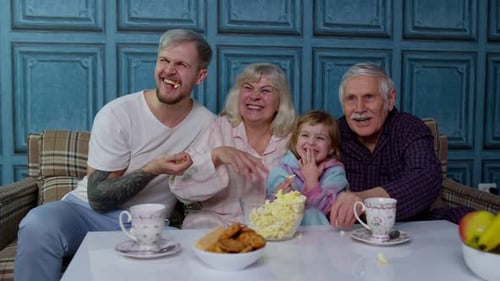 Familia multigeneracional: vea la televisión con una niña en casa riendo viendo una película de comedia de dibujos animados