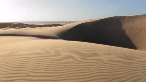 Drohnenaufnahme aus der Luft, die durch wunderschöne gewellte Sanddünen im goldenen Sonnenuntergangslicht fliegt