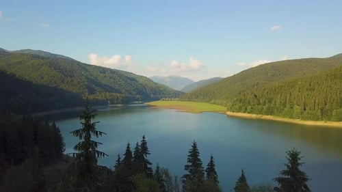 Aerial view of big lake with clear blue water between high mountain hills covered with dense