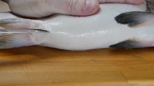 Der Koch schneidet den Bauch eines Fisches mit einem Messer auf einem Holzbrett