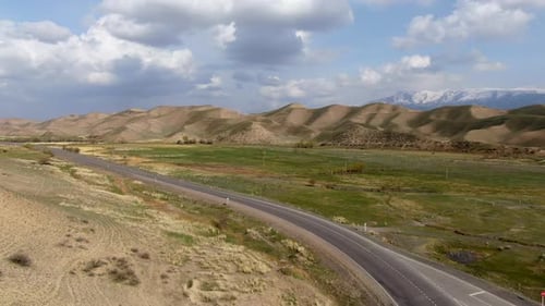 Aerial of highway in prairie with snowy summits of mountain in the background