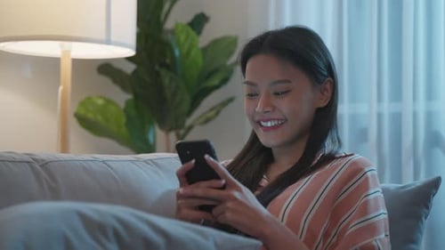 Asiatische schöne Frau sitzt auf dem Sofa und unterhält sich nachts mit dem Handy.