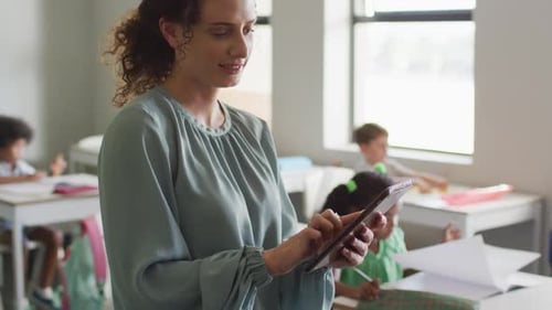 Video of happy caucasian female teacher using laptop at school during lessons