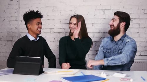Multiethnic Business Team Giving High Five Sitting at the Table in Modern Office