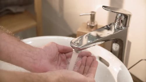 Close Up Of Hands Turn On Running Water In Sink In Bathroom
