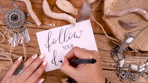 Woman's hand writing FOLLOW YOUR DREAM with bohemian decorations around