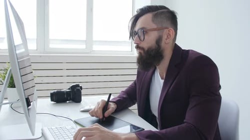 Bearded Man Uses Stylus and Tablet at Desk