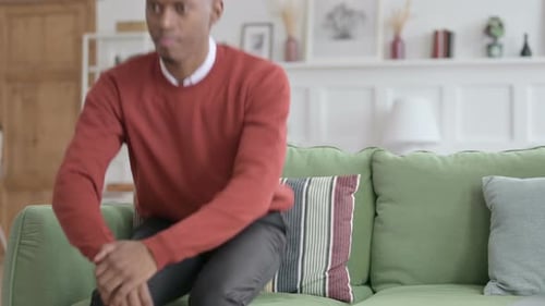 Young Man Sitting on Couch Stands Up
