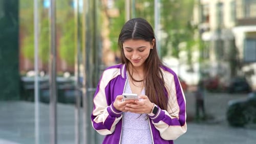 Happy Woman in the Street Using a Smartphone and Looking at Camera