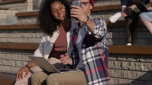 Friends Sitting with Laptop Smiling at Smartphone