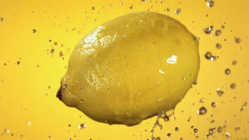 Lemon Falling Into Water on Yellow Background