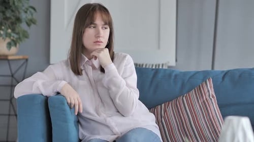 Young Woman Thoughtful Sitting on Sofa Indoors