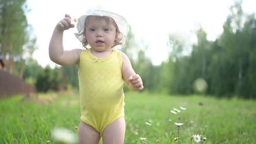 Little Funny Cute Blonde Girl Child Toddler in Yellow Bodysuit and White Hat Walking in Field with