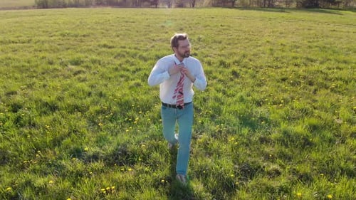 a Businessman Walking on a Green Field Takes Off Tie and Throws It Away
