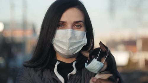 Woman in Protective Face Mask with Small Dog Wearing Medical Mask Too