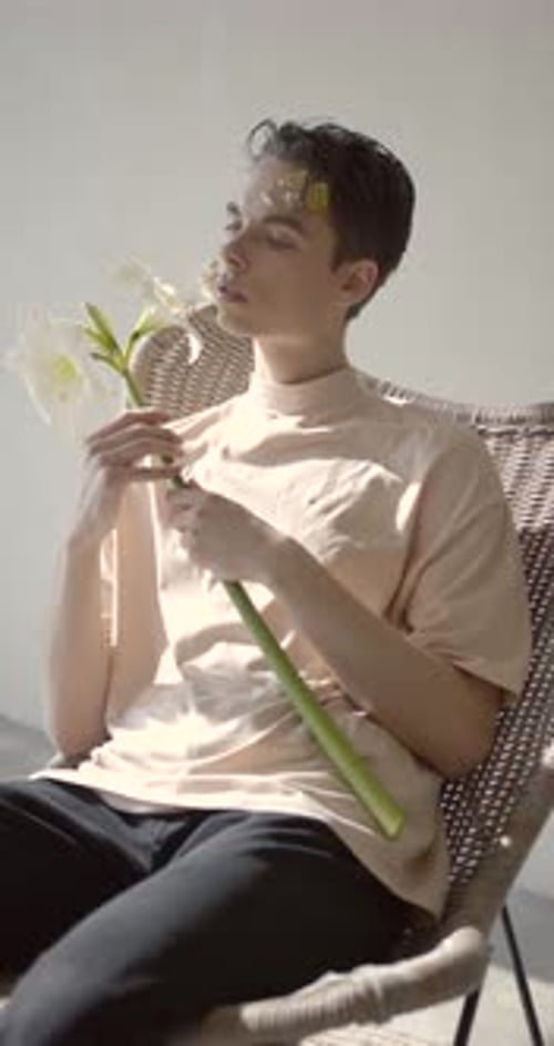 Young Man Holds White Flower in Woven Chair