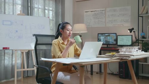 Asian Woman Engineer Drinking Coffee While Using A Laptop To Work At The Office
