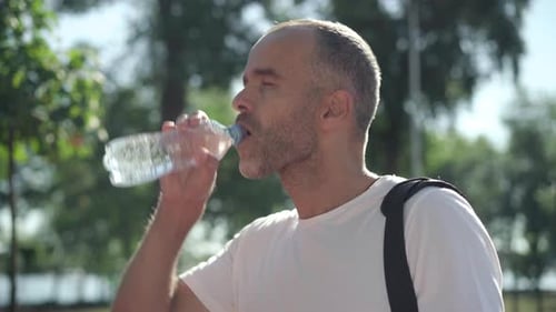 Close-up Side View of Handsome Adult Caucasian Man Drinking Water in Sunlight Outdoors and Smiling