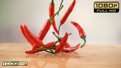 Red Chili Peppers Falling onto Wet Wooden Surface