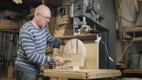 An Elderly Man in a Carpentry Workshop Saws Off the Remains of a Wooden Workpiece