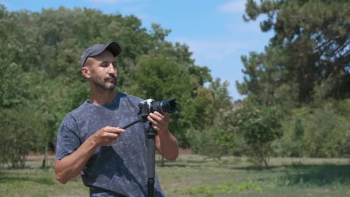 Man Adjusting Camera and Tripod in Park