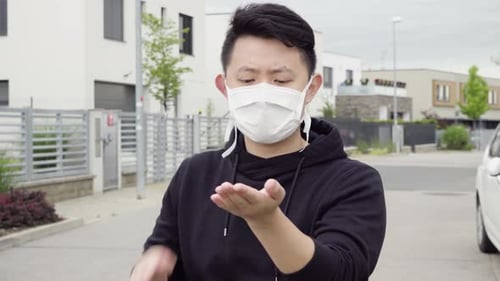 A Young Asian Man in a Face Mask Applies a Disinfection Gel on His Hands and Looks at the Camera