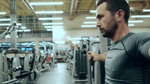 Modern Gym a Man Sitting Down on the Training Apparatus and Training