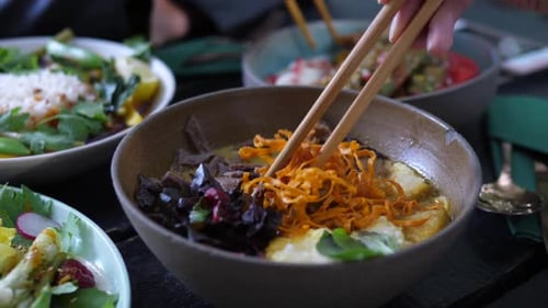 Primer plano de los palillos que mezclan los ingredientes en una sopa vegana saludable. Concepto de comida callejera asiática saludable