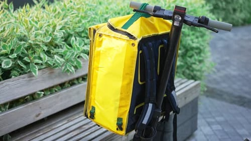 Mochila amarilla aislante para entrega de alimentos que cuelga del volante de Escoo
