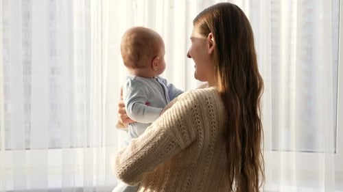 Mother Holds Baby in Arms near Window