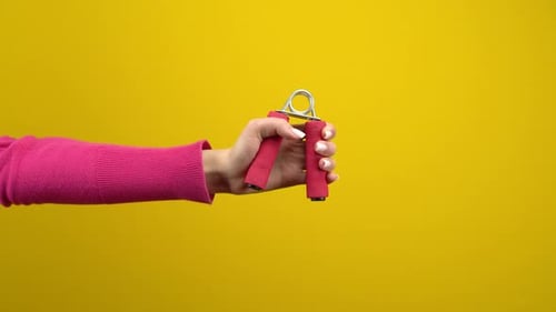 A Woman's Hand Squeezes a Pink Expander. Studio Photography on an Isolated Yellow Background
