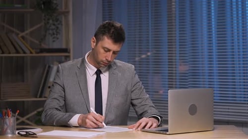 Professional Man Signing Documents in Office at Night