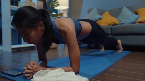 Mujer asiática en ropa deportiva haciendo ejercicio y usando el teléfono para ver un vídeo tutorial de yoga.