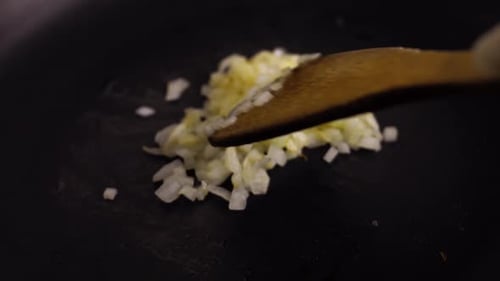 Onions sizzling in oil with wooden spoon