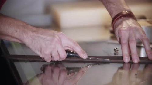 Der Schneider schneidet das Lederstück am Tisch mit einem scharfen Instrument ab