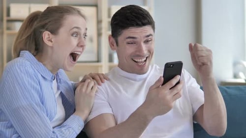 Couple Cheers While Looking at a Smartphone at Home