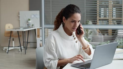Woman Working on Laptop, Talking on Phone in Office