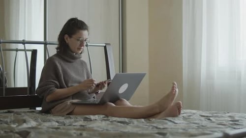 Woman Using Laptop and Phone on Bed