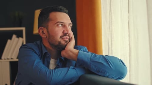 Man Gazing Out Window at Home, Deep in Thought