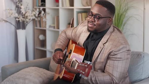 Man Plays Guitar on Couch in Living Room